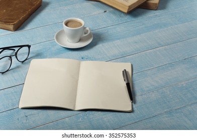 Home office table with open notebook with blank pages, a cup of espresso coffee and books. Top view with copy space
