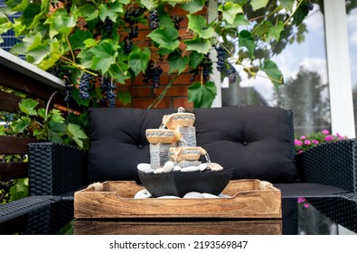 Home Patio With Black Plastic Garden Furniture, Small Relaxing Electrical Zen Table Fountain On Table And Real Grape Vines With Grapes Hanging On Background. Home Decor.