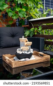 Home Patio With Black Plastic Garden Furniture, Small Relaxing Electrical Zen Table Fountain On Table And Real Grape Vines With Grapes Hanging On Background. Home Decor.