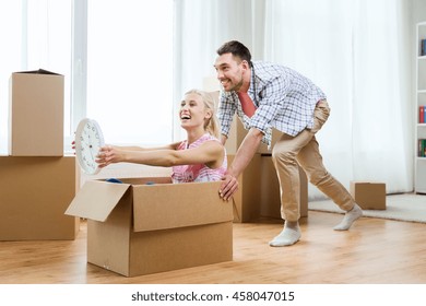 Home, People, Moving, Time And Real Estate Concept - Happy Couple Having Fun And Riding In Cardboard Boxes With Clock At New Home