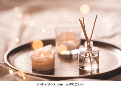 Home perfume in glass bottle with wood sticks, scented burn candles  tray in bedroom close up. Aromatherapy cozy atmosphere lifestyle. Winter warm xmas season.  - Shutterstock ID 2049128873