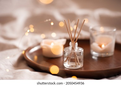 Home perfume in glass bottle with wood sticks, scented burn candles on tray in bedroom close up over white. Aromatherapy cozy atmosphere lifestyle. Winter warm xmas season. Good morning. 