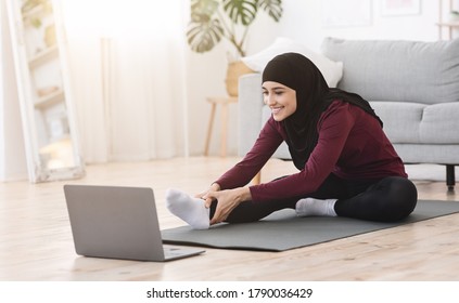 Home Pilates. Sporty arabic woman in hijab stretching leg muscles in front of laptop, watching online tutorials, copy space - Powered by Shutterstock