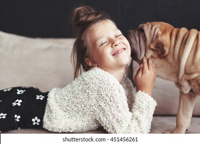 Home portrait of cute child hugging with puppy of Chinese Shar Pei dog on the sofa against black wall