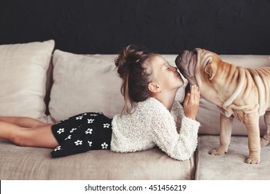 Home portrait of cute child kissing puppy of Chinese Shar Pei dog on the sofa against black wall - Powered by Shutterstock