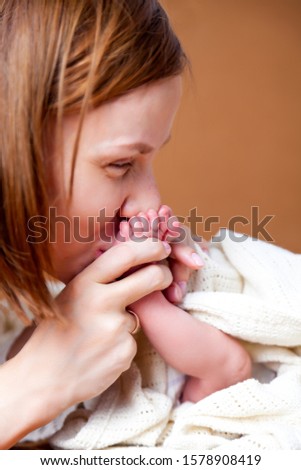Home portrait of mother, hands holding and kissing her child, sweet newborn baby pink cute feet. Concept of the long-awaited son, IVF, Cesarean section, natural birth, happy parenthood
