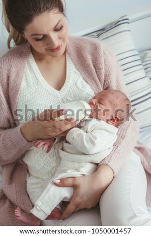 Home portrait of a newborn baby with mother on the bed. Young mom feeding her child from bottle.