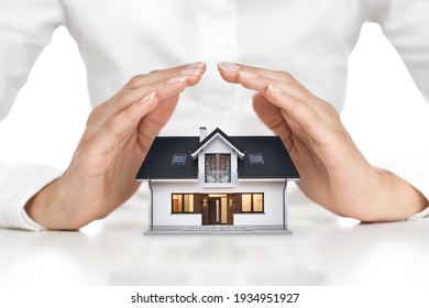 Home protection concept, close up of female hands sheltering modern house