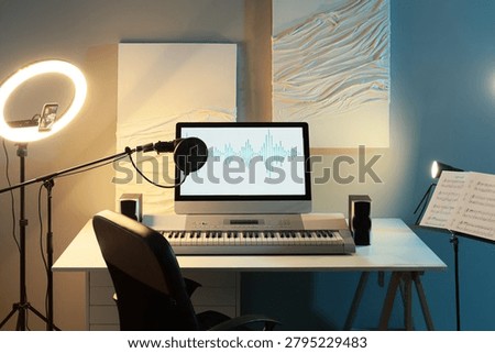Home recording studio setup with computer screen displaying audio waveform, microphone, keyboard, and ring light