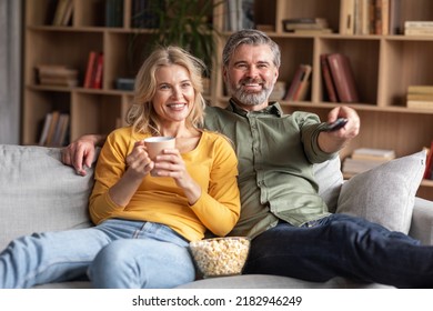 Home Relax. Happy Married Middle Aged Couple Watching Tv In Living Room, Smiling Spouses Eating Popcorn And Drinking Coffee Together While Relaxing On Comfortable Couch, Closeup Shot - Powered by Shutterstock