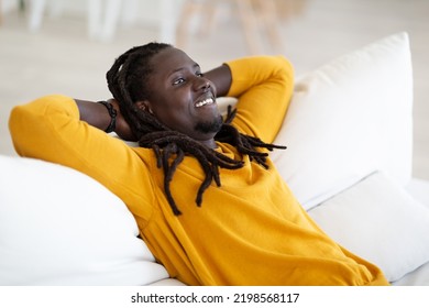 Home Relax. Smiling Black Guy Resting On Couch In Living Room, Dreamy African American Man With Dreadlocks Leaning Back On Sofa With Hands Behind Head, Enjoying Domestic Comfort, Free Space - Powered by Shutterstock