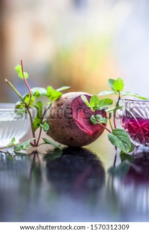 Home remedy for dandruff on wooden surface i.e., beetroot stock well mixed with water in a glass bowl along with some freshwater and raw sliced beetroot. Vertical shot with blurred creamy bokeh.
