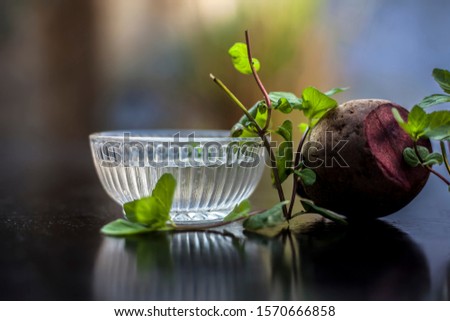 Home remedy for dandruff on wooden surface i.e., beetroot stock well mixed with water in a glass bowl along with some freshwater and raw sliced beetroot. Horizontal shot with blurred creamy bokeh.