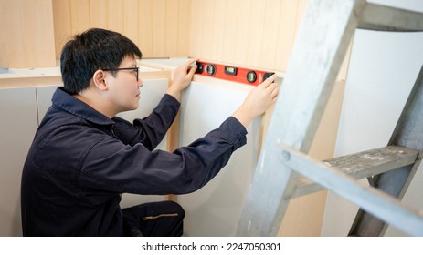 Home renovation or House remodeling concept. Asian male furniture assembler or Interior construction worker man using spirit level tool installing wooden counter and cabinet of new kitchen. - Powered by Shutterstock