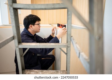 Home renovation or House remodeling concept. Asian male furniture assembler or Interior construction worker man using spirit level tool installing wooden counter and cabinet of new kitchen. - Powered by Shutterstock