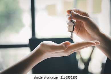 A home rental company employee is handing the house keys to a customer who has agreed to sign a rental contract, explaining the details and terms of the rental. Home and real estate rental ideas. - Shutterstock ID 2166555255