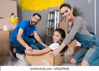 Home Repair. Moving Young Family To New Apartment. Repair In House For Sale. Happy Couple Carries Small Daughter In Box At House Where Repairs Are Being Carried Out.