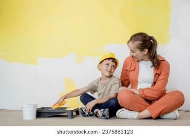 Home repairs. Mom helping her son paint the wall with a roller. The boy paints the wall of the apartment. New house renovation concept - Powered by Shutterstock