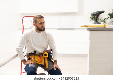 Home repairs. Portrait of professional male repairman with metal ladder. Smiling man in work overalls stands in middle of room in which he has finished making repairs. - Powered by Shutterstock