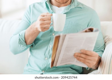 Home, Rest, News, Drinks And People Concept - Close Up Of Man Reading Magazine And Drinking From Cup Sitting On Couch At Home