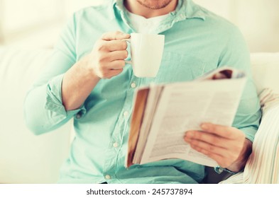 Home, Rest, News, Drinks And People Concept - Close Up Of Man Reading Magazine And Drinking From Cup Sitting On Couch At Home