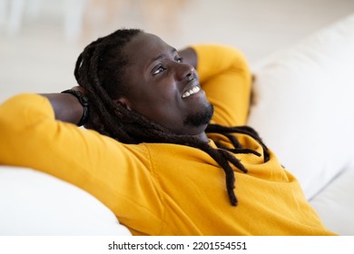 Home Rest. Portrait Of Smiling Young Black Man Leaning Back On Couch, Dreamy African American Male Sitting On Sofa With Hands Behind Back, Millenial Guy Relaxing In Living Room, Closeup Shot