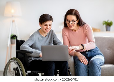 Home Schooling Concept. Disabled Teen Boy In Wheelchair Studying New Online Materials Together With His Mother Indoors. Handicapped Teenager And Private Tutor Doing Assignment On Laptop