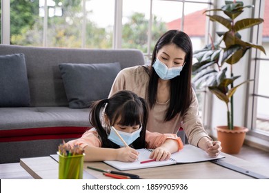 Home schooling learning at home during virus pandemic. asian woman with her daughter in the living room , wearing surgical face masks to protect them from the virus.
