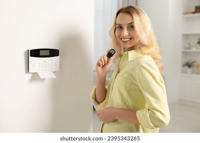 Home security system. Smiling woman with alarm key fob in room - Shutterstock ID 2395343265