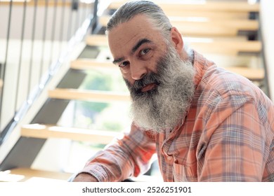 At home, Senior man with long beard sitting on stairs, looking at camera. Portrait, mature, contemplation, lifestyle, bearded, candid, unaltered - Powered by Shutterstock