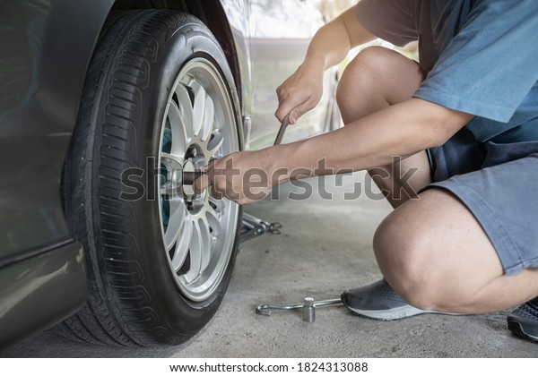 Home service car concept : A man\
repairing action remove bolt of car wheel for check the car\'s drive\
system basic maintenance that can be made by\
yourself