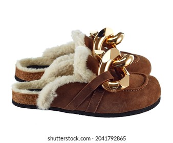 Home slippers with an open heel, made of natural sheepskin, fur inside, brown suede outside, decorated with large links of a gold chain isolated on a white background. Side view. Fashionable shoes.