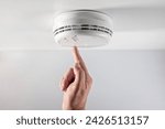 Home smoke and fire alarm detector maintenance man pushing button checking, testing or replacing battery