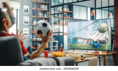 At Home Soccer Fans Sitting On A Couch Watch Football Game On TV, Cheer For Favourtite Sports Team To Win Championship. Screen Shows Professional Football Club Play. Over The Shoulder