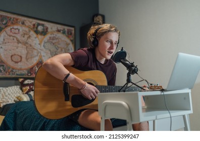 Home Sound Studio Young Teenager Portrait Playing Guitar In Headphones Recording Voice Music Using A Microphone And Laptop Computer In The Kids Room. Modern Audio Recording Technology Concept Image.