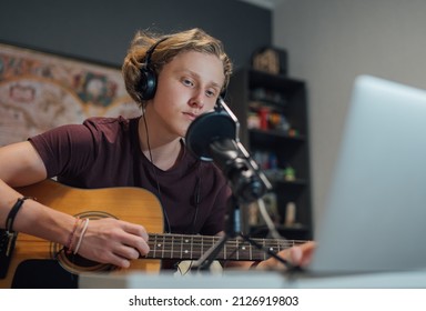 Home Sound Studio Young Teenager Portrait Playing Guitar In Headphones Recording Voice Music Using A Microphone And Laptop Computer In The Kids Room. Modern Audio Recording Technology Concept Image.