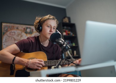 Home Sound Studio Young Teenager Portrait Playing Guitar In Headphones Recording Voice Music Using A Microphone And Laptop Computer In The Kids Room. Modern Audio Recording Technology Concept Image.