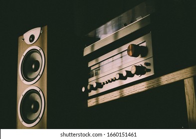 Home Sound System - Wooden Speaker With Two White Membrane Drivers, Vintage Stereo Receiver And Turntable Placed On The Top Of It. Audio Equipment Stands On The Wooden Shelf. Heavy Shadow Scene.