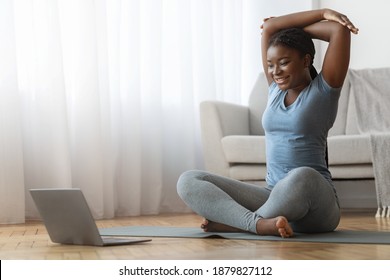 Home Sport. Fit young black lady watching online tutorials on laptop and training on yoga mat in living room, stretching arm muscles and smiling, enjoying fitness and healthy lifestyle, copy space - Powered by Shutterstock