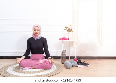 Home Sports. Active fit asian muslim lady in hijab doing yoga with close her eyes, training on fitness mat in living room, copy space - Powered by Shutterstock