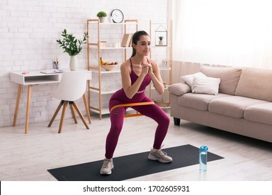Home sports concept. Hispanic girl doing squats with elastic band in living room