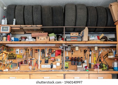 Home Suburban Garage Interior Big Wooden Workbench With Lot Of Power Mechanic Tools At Background. Spare Season Wheels Storage Shelf Rack Ceiling Warehouse. DIY, Self Service And Repair