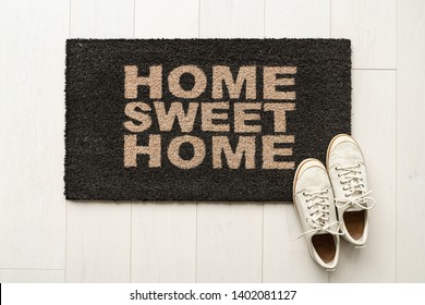 Home sweet home door mat at house entrance with women's sneakers of woman that has just arrived moved in. New condo.