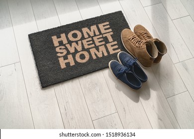 Home Sweet Home Doormat At Condo Door Entrance With Couples Pairs Of Shoes Moving In Together. Women's Sneakers And Man's Boots On Floor, New Apartment.