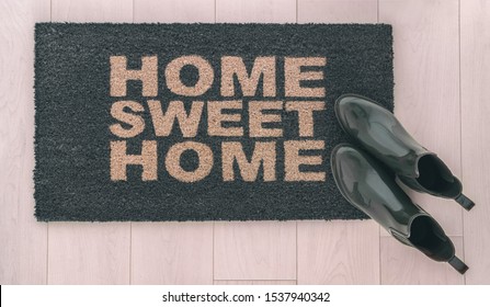 Home Sweet Home Doormat Entrance Mat At Front Door Of New Condo In Urban City Living With Stylish Womens Rain Boots Of Homeowner Resting On Top.