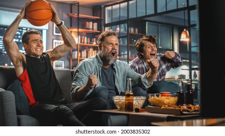 At Home Three Joyful Basketball Fans Sitting On A Couch Watch Game On TV, Celebrate Victory When Sports Team Wins Championship. Group Of Friends Cheer When Favourites Play.