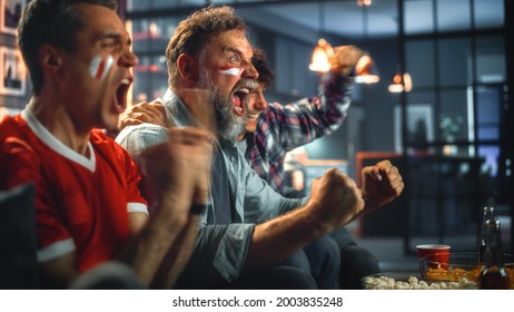 At Home Three Joyfuls Sports Fans with Painted Faces Sitting on a Couch Watch Game on TV, Celebrate Victory when Sports Team Wins Championship. Friends Cheer, Shout. - Shutterstock ID 2003835248