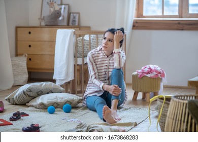 At Home. Tired Woman Sitting On The Floor In Messy Room, Propping Up Her Head