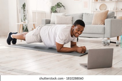 Home Training. Black Man Exercising Doing Plank Exercise At Laptop During Online Workout Indoors