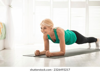 Home training concept. Smiling senior woman doing elbow plank on yoga mat in living room, sporty mature lady doing fitness workout routine, exercising indoors, strengthening her core muscles - Powered by Shutterstock